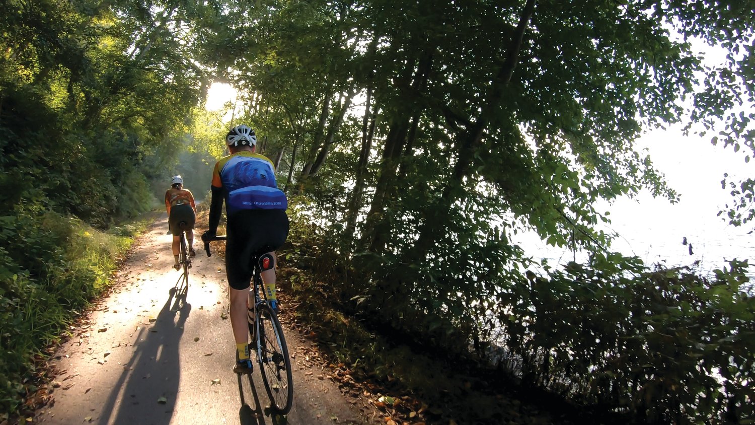 Sunlight filters through the trees as cyclists make their way along the trail.